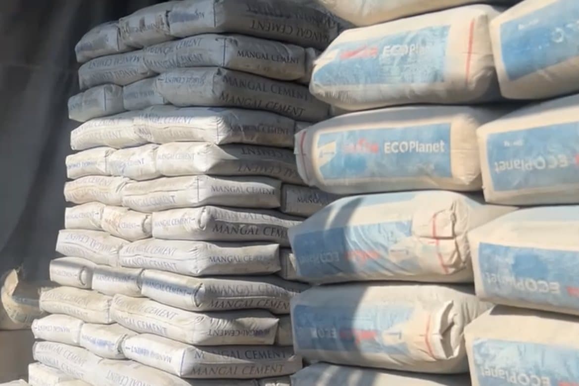 Cement bags from two different makers stacked side by side in a depot.